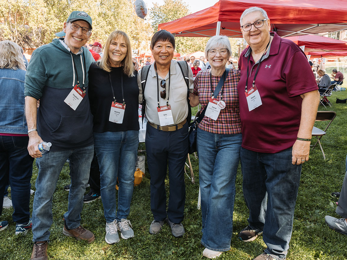 A group of five alumni from 1975 pose for a photo at a tailgate